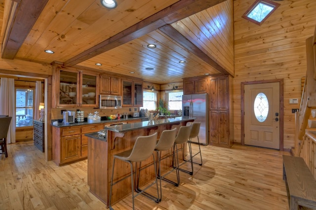 kitchen with a center island, wooden ceiling, stainless steel appliances, wooden walls, and light wood-type flooring