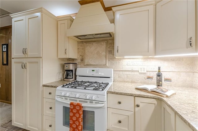 kitchen featuring light stone countertops, custom range hood, white gas range oven, and backsplash