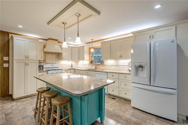 kitchen featuring white appliances, light stone counters, a center island, hanging light fixtures, and stone finish flooring