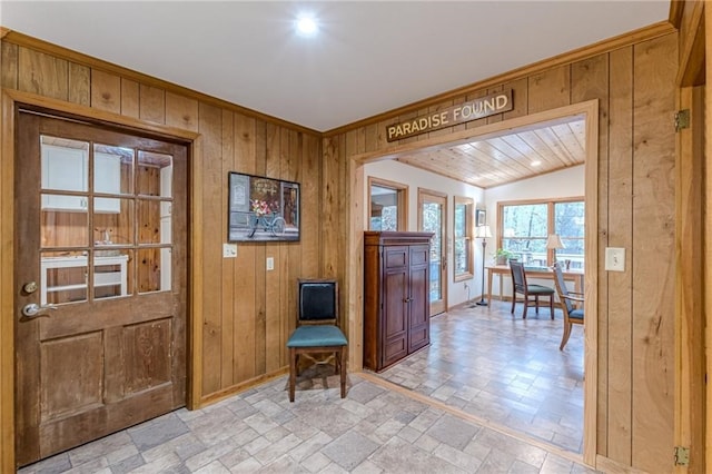 foyer entrance featuring stone finish flooring, crown molding, wooden walls, and baseboards