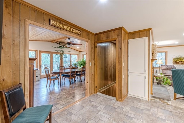 dining space featuring ceiling fan, lofted ceiling, wooden walls, stone finish flooring, and crown molding