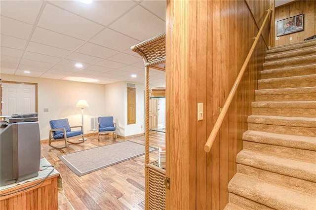 staircase with recessed lighting, visible vents, wooden walls, wood finished floors, and a drop ceiling