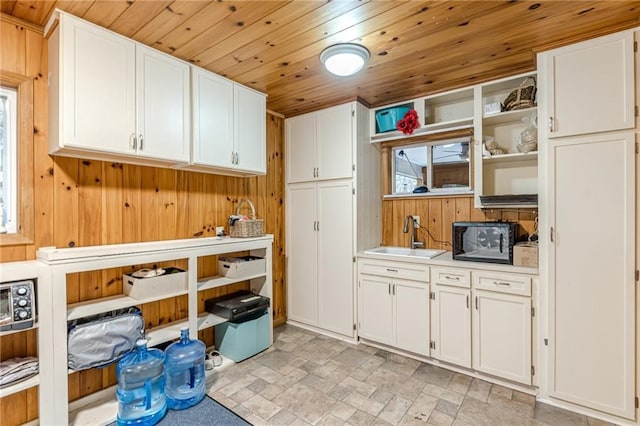 kitchen featuring light countertops, wood ceiling, white cabinetry, a sink, and wood walls