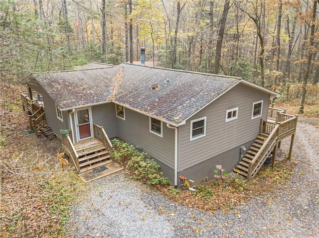 chalet / cabin featuring gravel driveway, a shingled roof, and stairs