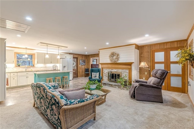 living area featuring ornamental molding, a stone fireplace, french doors, and wood walls