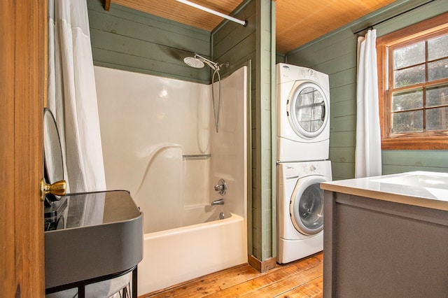 clothes washing area featuring wood walls, wooden ceiling, stacked washer and clothes dryer, sink, and light wood-type flooring