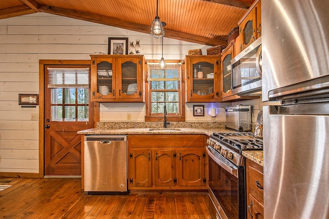 kitchen featuring decorative light fixtures, lofted ceiling with beams, light stone counters, and appliances with stainless steel finishes