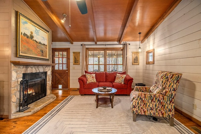 living room with lofted ceiling with beams, a stone fireplace, wooden walls, hardwood / wood-style flooring, and ceiling fan