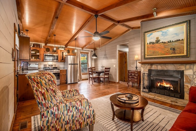 living room with sink, light hardwood / wood-style flooring, a fireplace, vaulted ceiling with beams, and wood walls