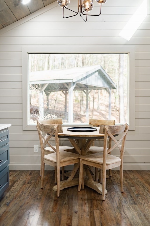 dining area featuring dark wood-type flooring, wooden walls, a chandelier, and lofted ceiling