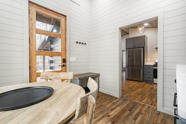 dining space featuring dark wood-type flooring, wooden walls, and high vaulted ceiling