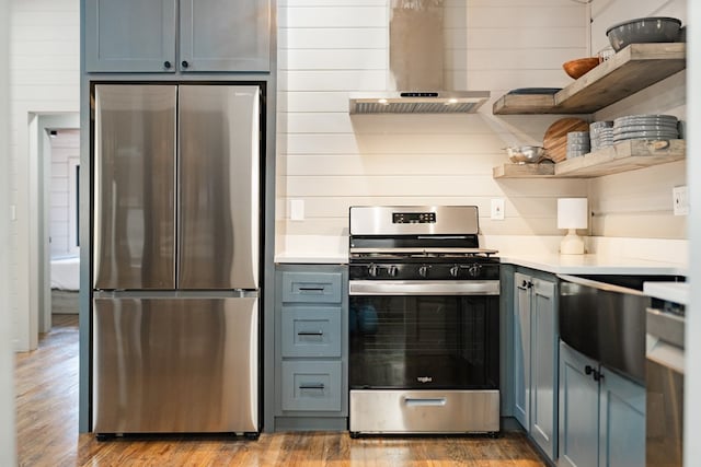 kitchen featuring island exhaust hood, blue cabinetry, appliances with stainless steel finishes, wooden walls, and light hardwood / wood-style floors