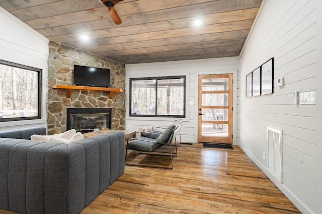 living room featuring a stone fireplace, wood walls, hardwood / wood-style flooring, lofted ceiling, and wooden ceiling