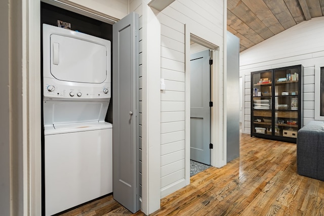 laundry room with stacked washer / drying machine, wooden walls, and hardwood / wood-style floors