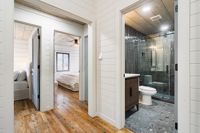 bathroom featuring hardwood / wood-style flooring, an enclosed shower, wooden walls, and toilet