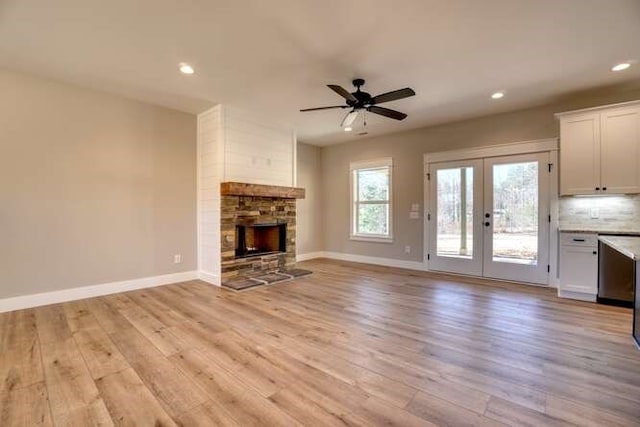 unfurnished living room with a fireplace, ceiling fan, light hardwood / wood-style flooring, and french doors