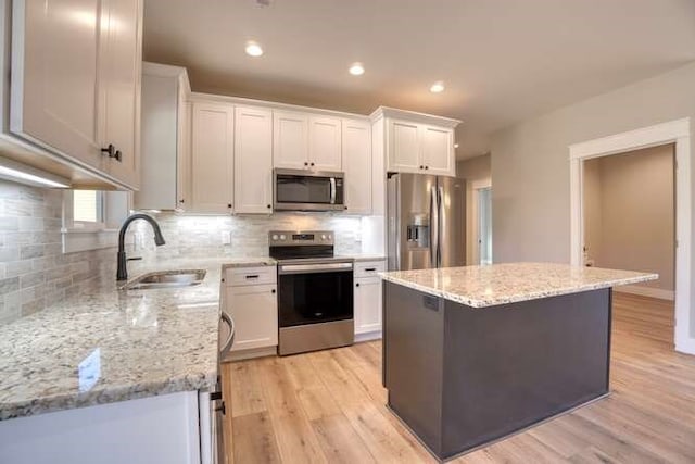 kitchen with white cabinetry, sink, stainless steel appliances, light hardwood / wood-style flooring, and a kitchen island