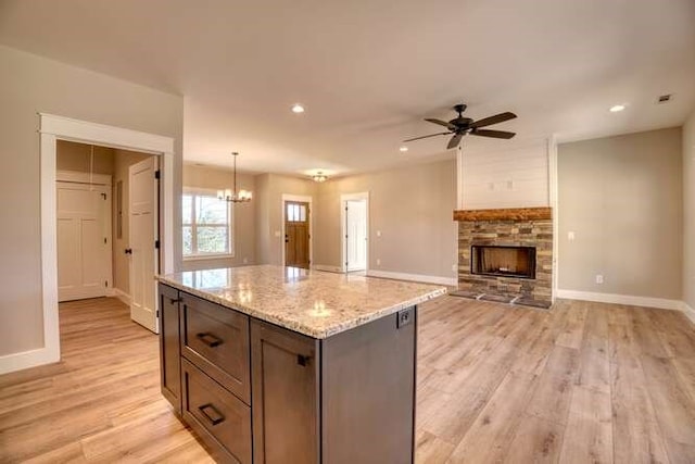 kitchen with ceiling fan with notable chandelier, decorative light fixtures, light hardwood / wood-style flooring, a kitchen island, and a stone fireplace