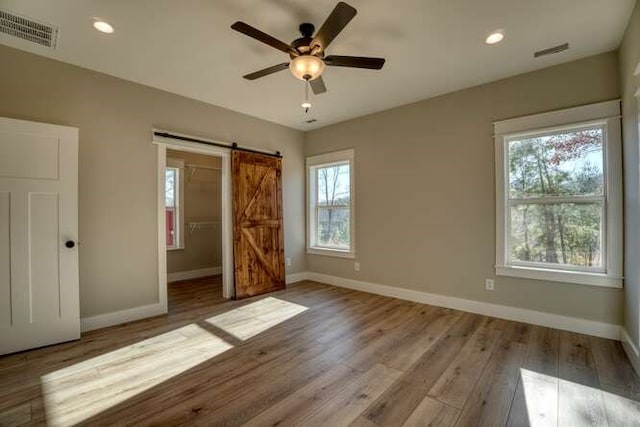 unfurnished bedroom featuring ceiling fan, a barn door, light hardwood / wood-style floors, and multiple windows