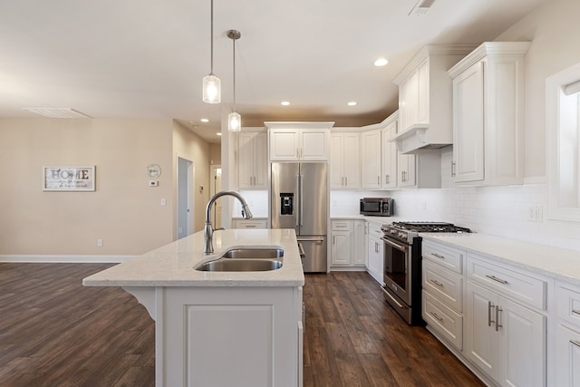 kitchen featuring dark wood-style floors, a center island with sink, a sink, decorative backsplash, and premium appliances