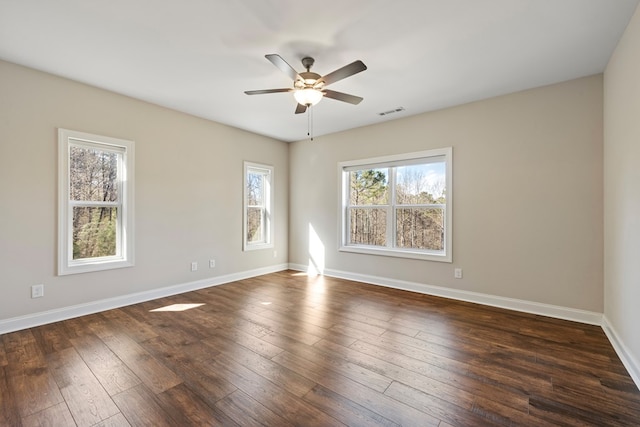 unfurnished room with a wealth of natural light, visible vents, dark wood-type flooring, and baseboards