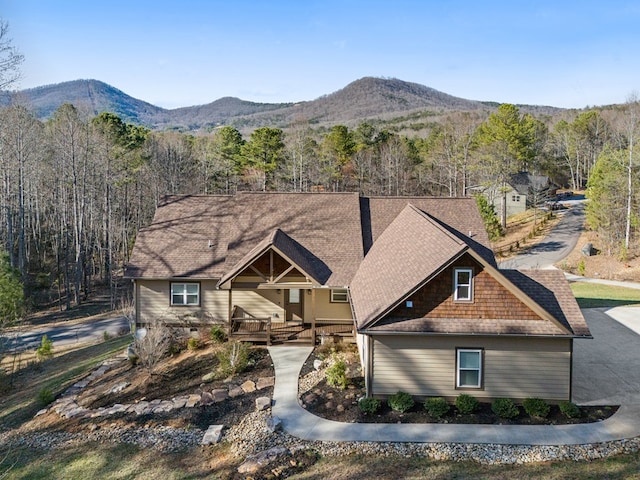 view of front facade with a mountain view, a forest view, and a shingled roof