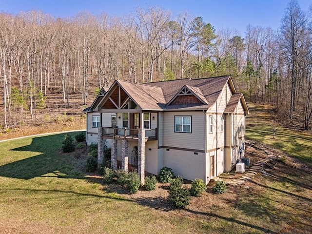 view of front of property featuring a front yard, a balcony, a forest view, and central AC