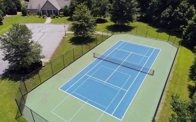 view of tennis court with a lawn and fence