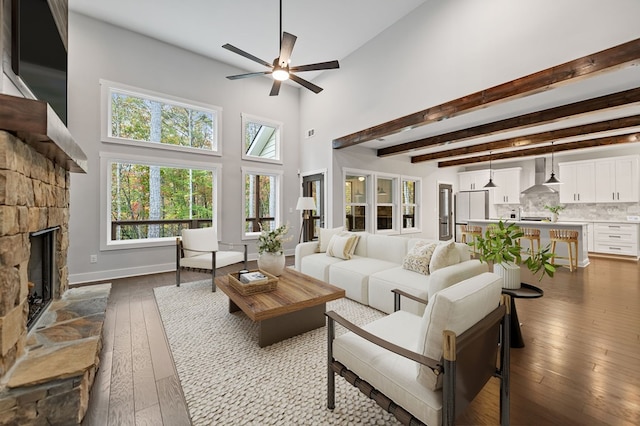 living room with light wood-type flooring, a fireplace, ceiling fan, beamed ceiling, and a high ceiling