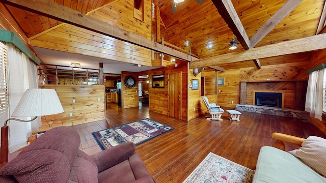 living area featuring a ceiling fan, a fireplace, wood walls, wood-type flooring, and beamed ceiling