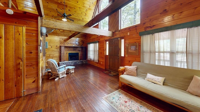 living area featuring a fireplace, beamed ceiling, ceiling fan, wooden walls, and hardwood / wood-style flooring