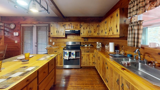 kitchen featuring wood walls, dark wood-style floors, under cabinet range hood, a sink, and double oven range