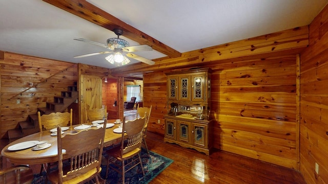 dining space with wooden walls, ceiling fan, beam ceiling, and wood-type flooring