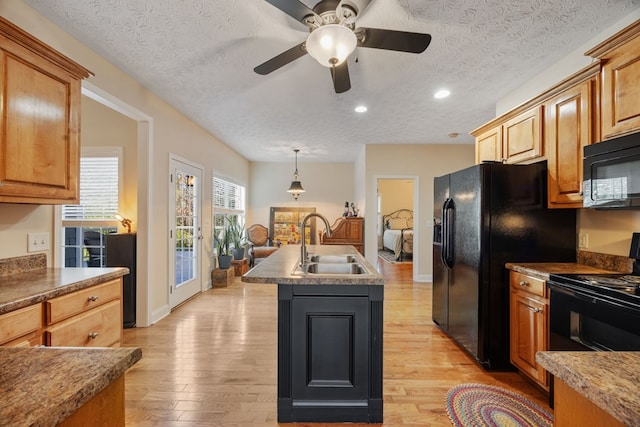 kitchen featuring sink, a textured ceiling, a kitchen island with sink, light hardwood / wood-style flooring, and black appliances