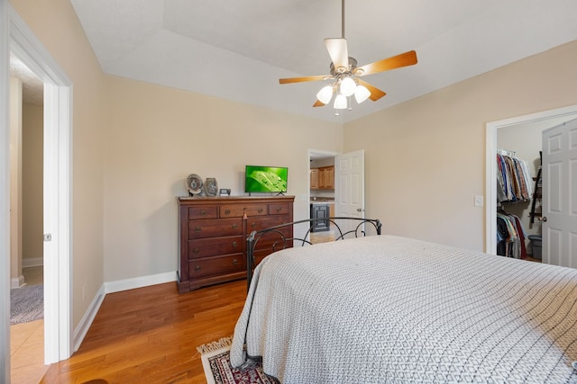 bedroom featuring ceiling fan, light hardwood / wood-style floors, a closet, a walk in closet, and a tray ceiling