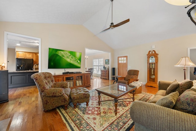 living room featuring ceiling fan, light wood-type flooring, vaulted ceiling, and sink