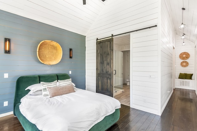 bedroom featuring visible vents, wood walls, hardwood / wood-style floors, a barn door, and vaulted ceiling