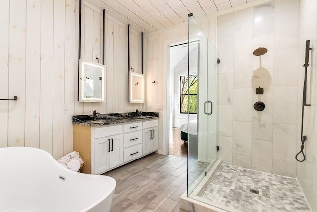 bathroom featuring double vanity, a freestanding tub, a shower stall, wood finished floors, and a sink