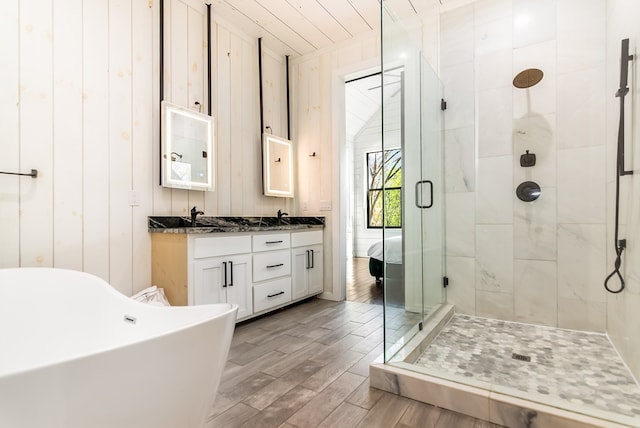 bathroom with double vanity, a shower stall, wood finished floors, a sink, and a soaking tub