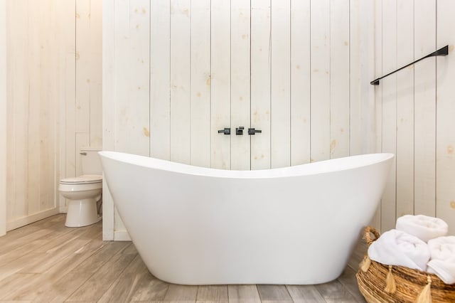 full bath with a soaking tub, toilet, wood walls, and wood finished floors