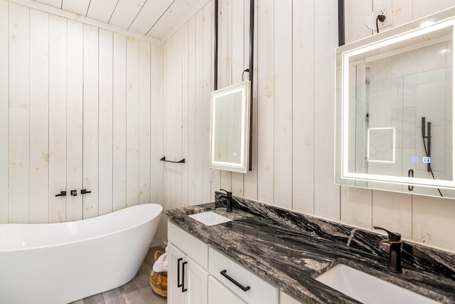 full bathroom with a freestanding bath, a sink, double vanity, wood walls, and a stall shower