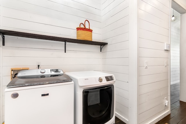 clothes washing area featuring washer and dryer, wooden walls, laundry area, and dark wood-type flooring