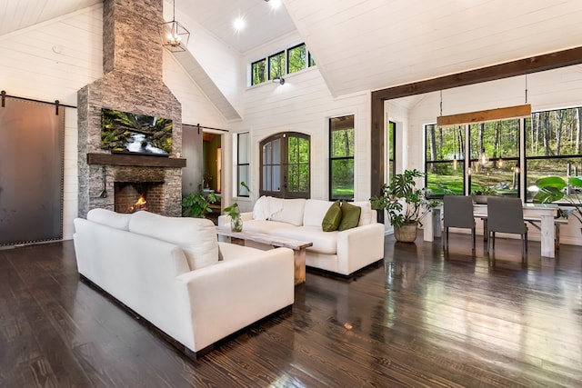 living room featuring a barn door, high vaulted ceiling, a stone fireplace, beamed ceiling, and hardwood / wood-style flooring