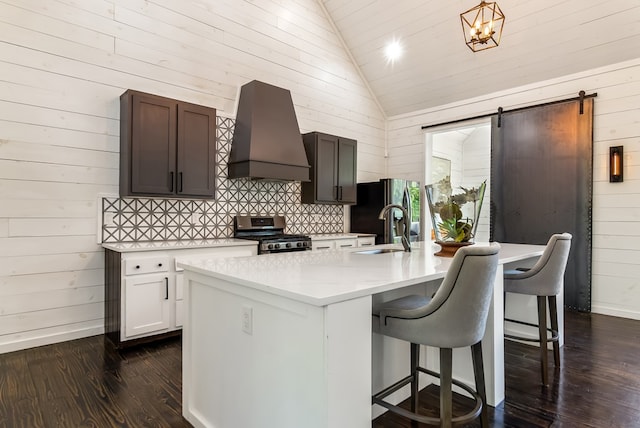 kitchen featuring wood walls, lofted ceiling, custom exhaust hood, light countertops, and appliances with stainless steel finishes