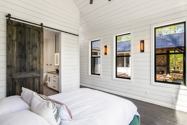 bedroom featuring a barn door, dark wood-style flooring, multiple windows, and wood walls