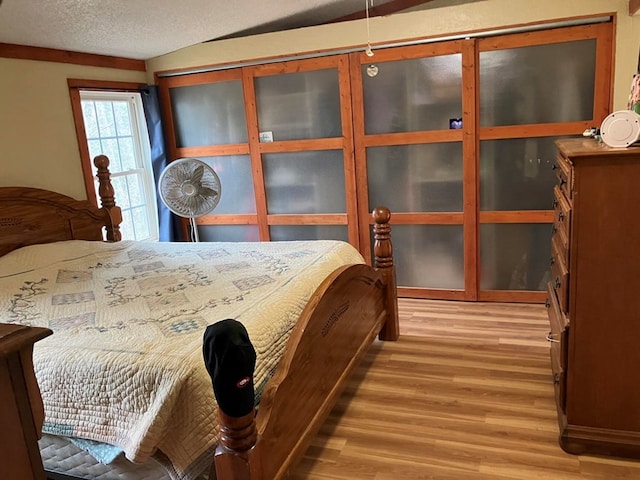 bedroom featuring lofted ceiling, a textured ceiling, and light hardwood / wood-style flooring