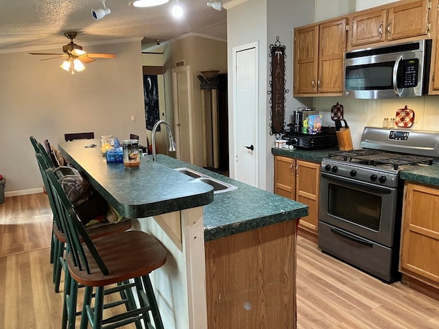 kitchen featuring stainless steel appliances, a textured ceiling, a breakfast bar area, a kitchen island with sink, and ornamental molding