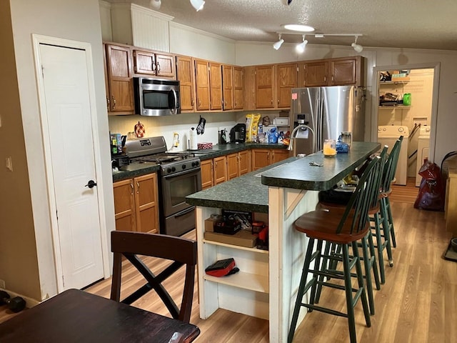 kitchen with a kitchen island with sink, a textured ceiling, a kitchen bar, stainless steel appliances, and washing machine and clothes dryer