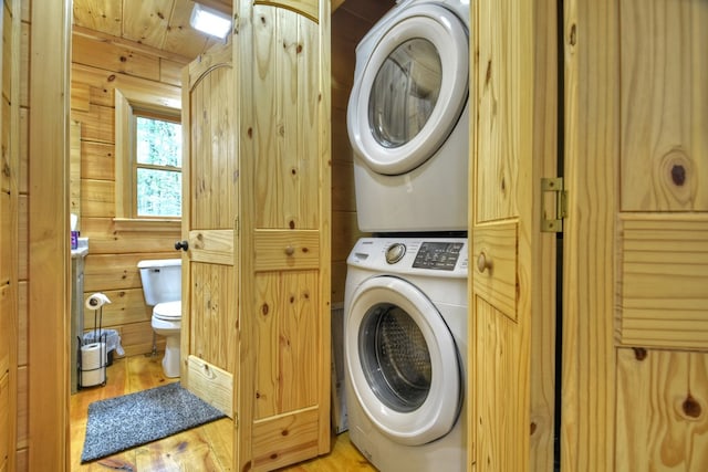 laundry room featuring wooden walls, light hardwood / wood-style flooring, stacked washer / drying machine, and wood ceiling