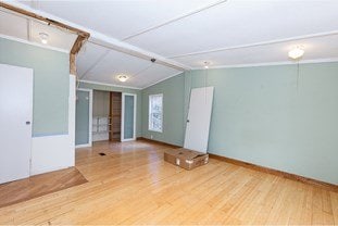 empty room featuring lofted ceiling with beams, baseboards, and wood finished floors